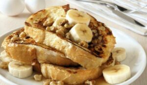 Golden-brown French toast topped with sliced bananas and granola served on a white plate.
