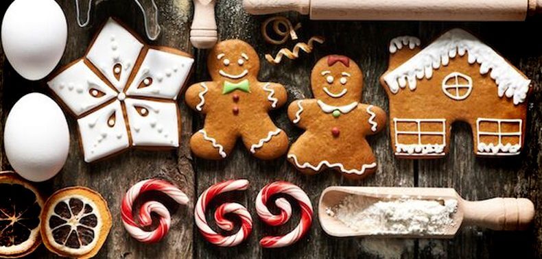Gingerbread cookies, including decorated gingerbread men and a house, are arranged on a wooden surface alongside eggs, peppermint candy, dried orange slices, and a rolling pin.