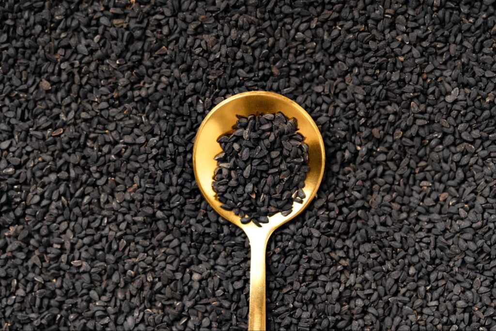 A large amount of black seeds with spoon in it scooping some out