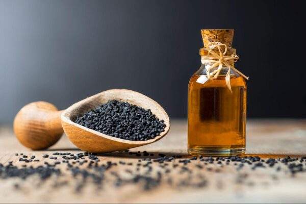 A wooden scoop full of black seeds near a small bottle of black seed oil