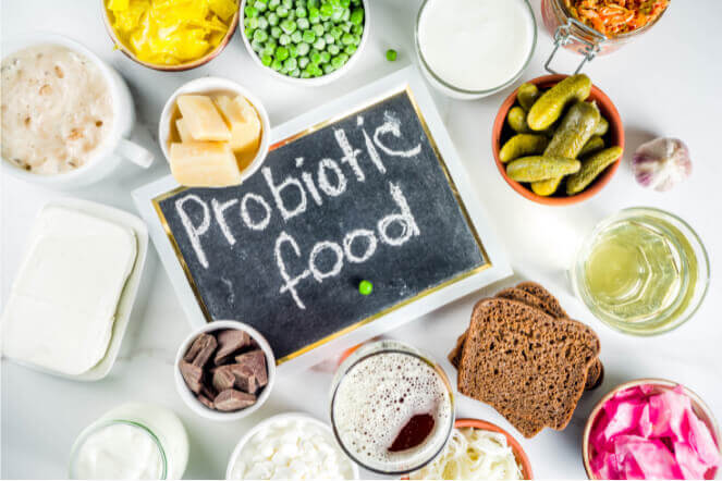 An assortment of probiotic foods is displayed around a chalkboard that reads "Probiotic food," featuring items like yogurt, pickles, sauerkraut, and various vegetables.