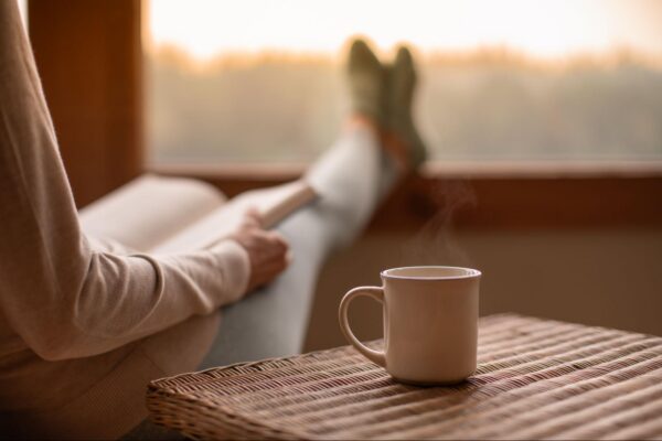 A woman reading a book drinking a steaming cup of coffee