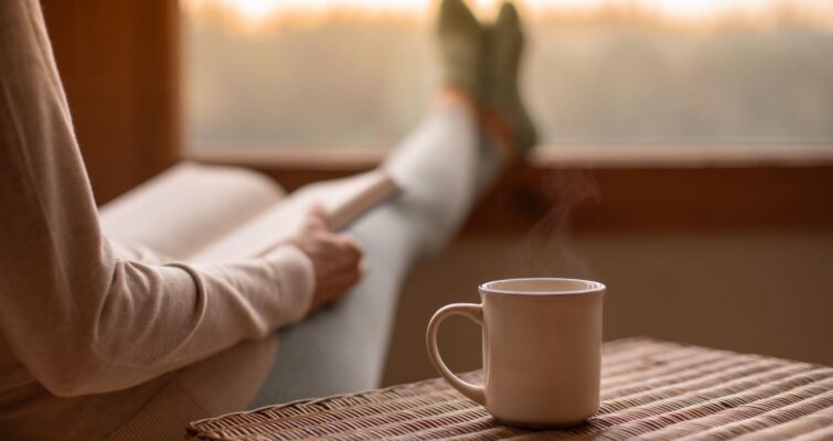 A woman reading a book drinking a steaming cup of coffee