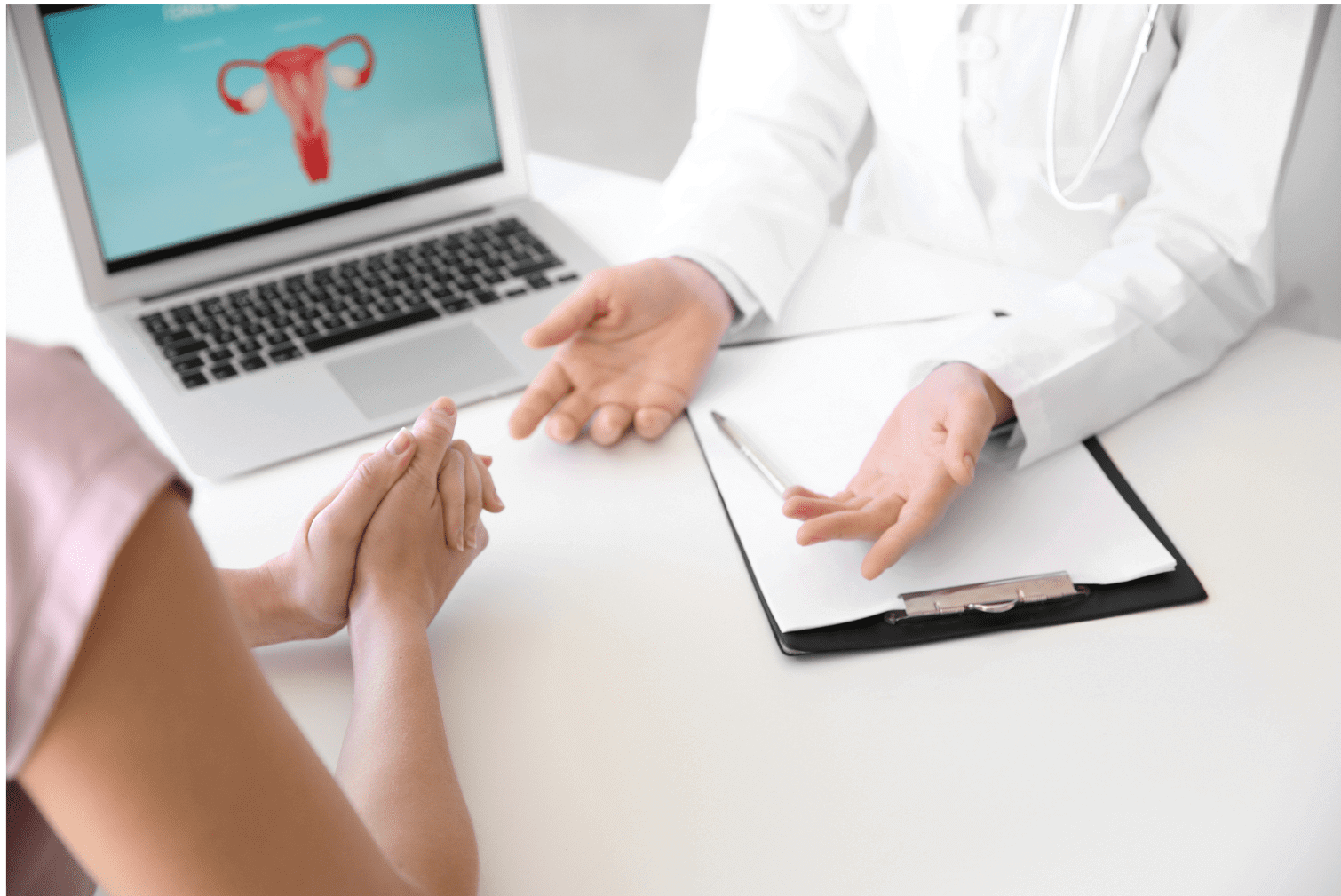 A healthcare provider in a white coat discusses reproductive health with a patient while a laptop displays a uterus diagram.