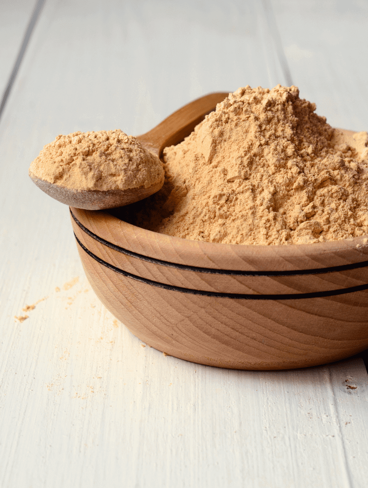 Ground cinnamon powder in a wooden bowl with a wooden scoop on a white surface.