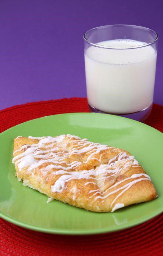 A piece of glazed pastry is placed on a green plate next to a glass of milk.