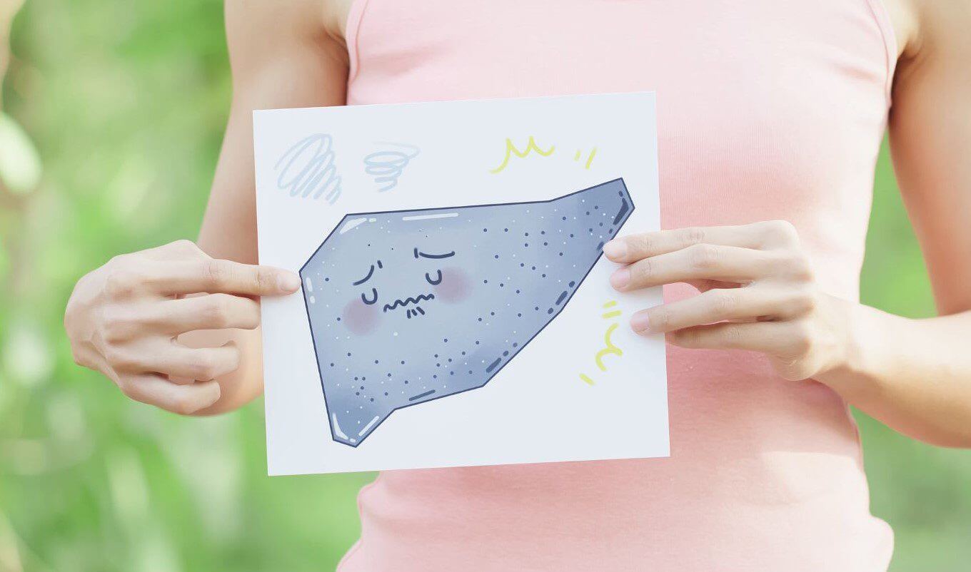 A person in a pink shirt holds a drawing of a sad, cartoonish rock with a blurred green background.