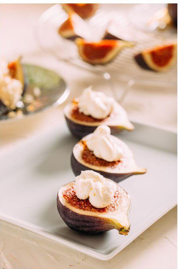 Roasted fig halves topped with whipped cream and dusted with cinnamon arranged on a white plate.