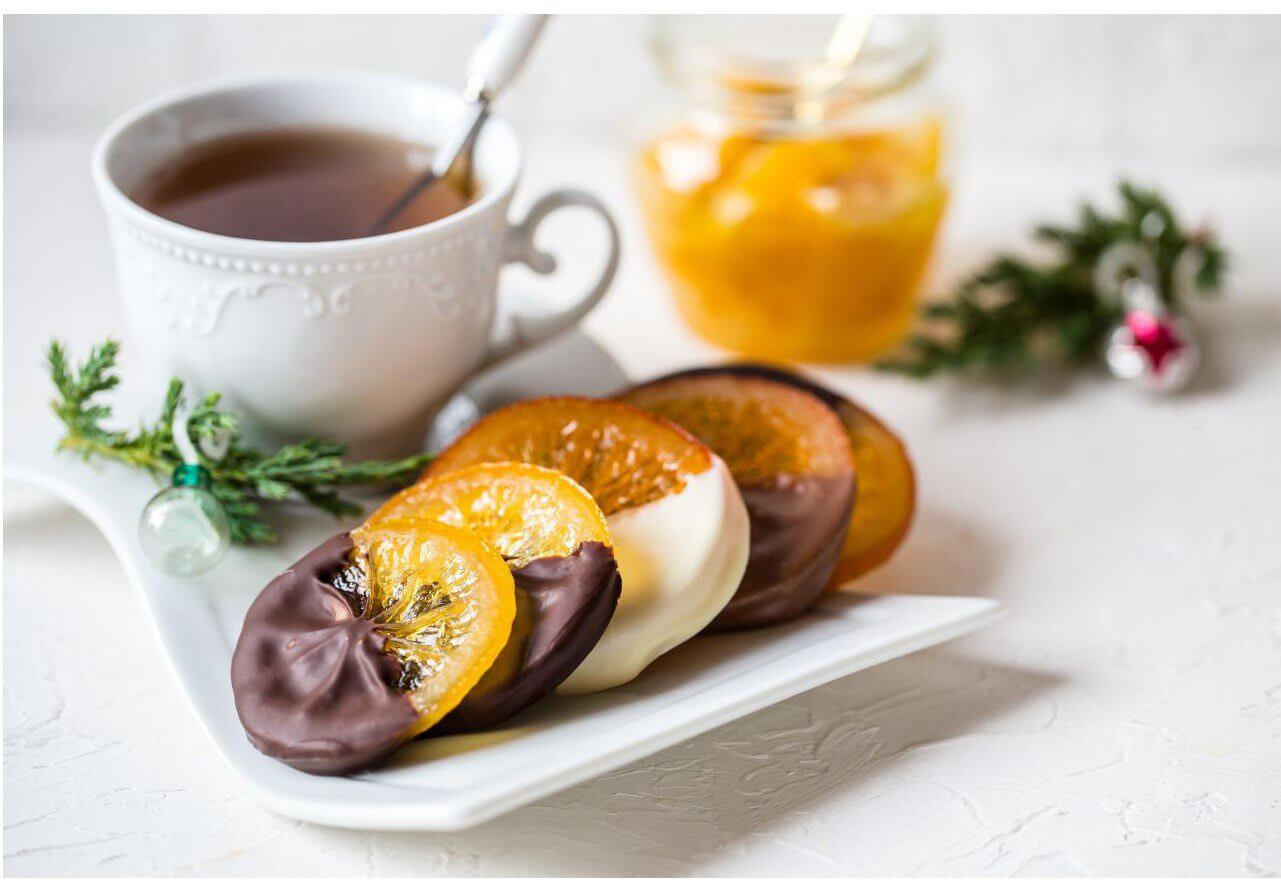 A plate of chocolate-covered oranges next to a cup of tea, showcasing a delightful snack pairing.