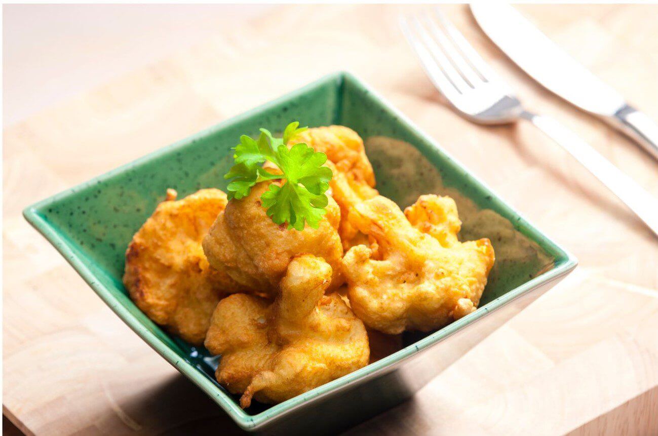 A bowl filled with various fried foods, accompanied by a fork and knife resting beside it.