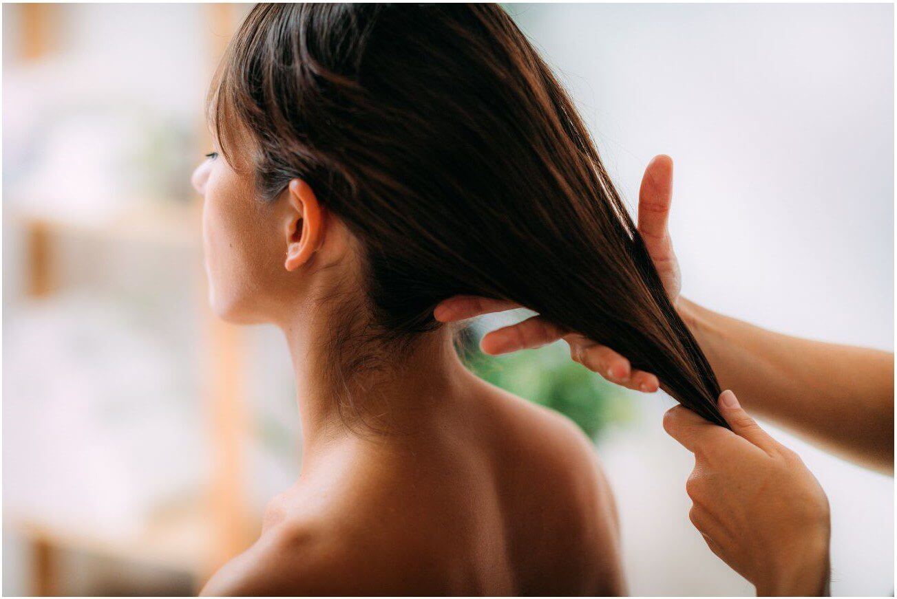 A person with long, dark hair is having their hair gently pulled back by another person.