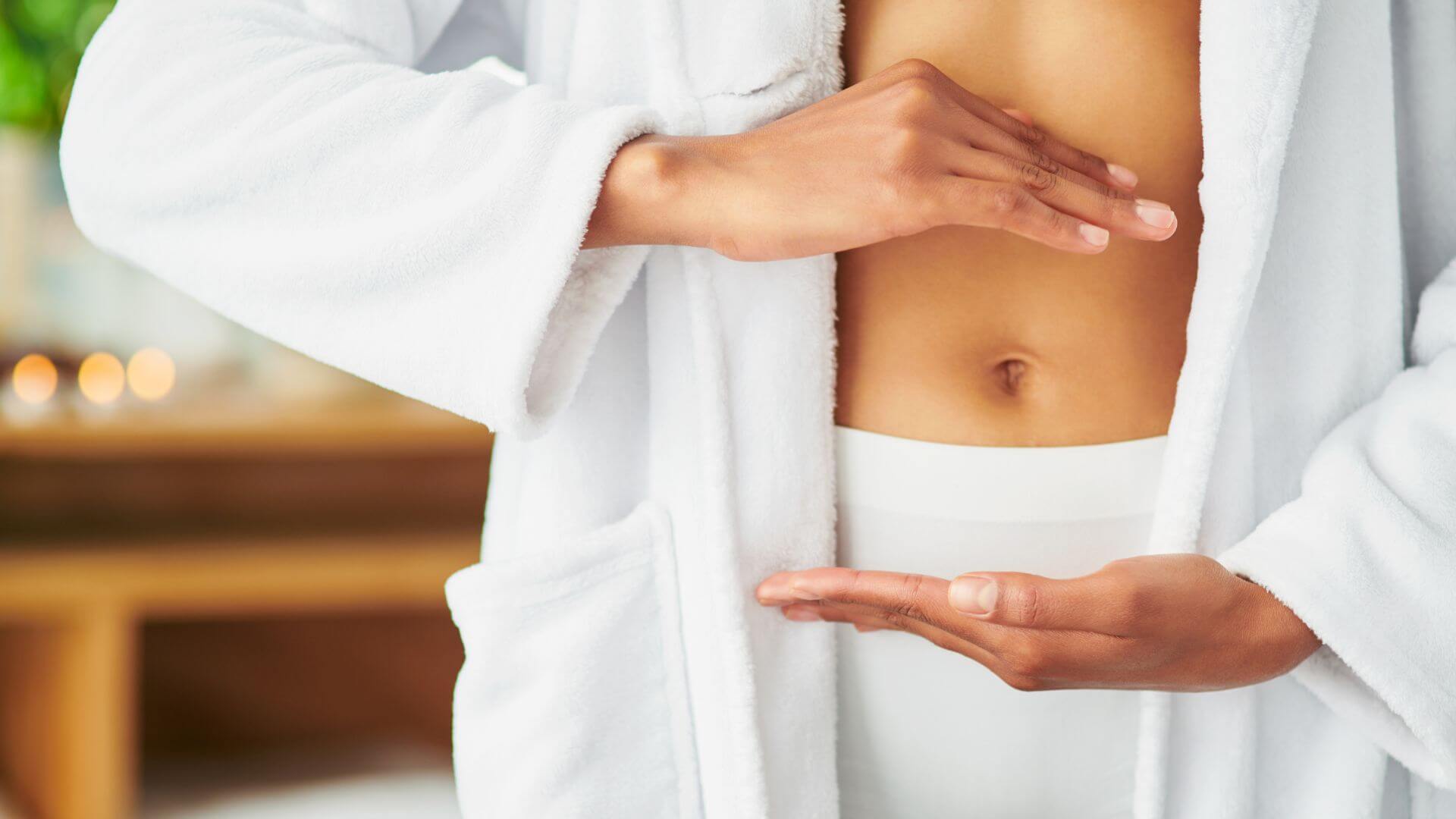 A woman in a robe gently touches her stomach, conveying a sense of contemplation or comfort.
