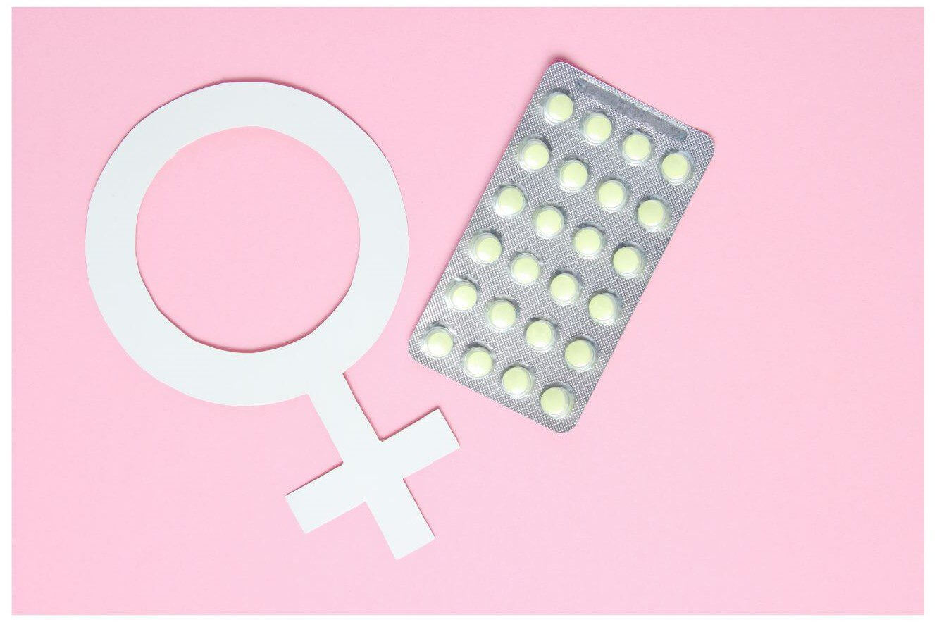 A paper symbol representing femininity is positioned next to a blister pack containing yellow tablets on a pink background.
