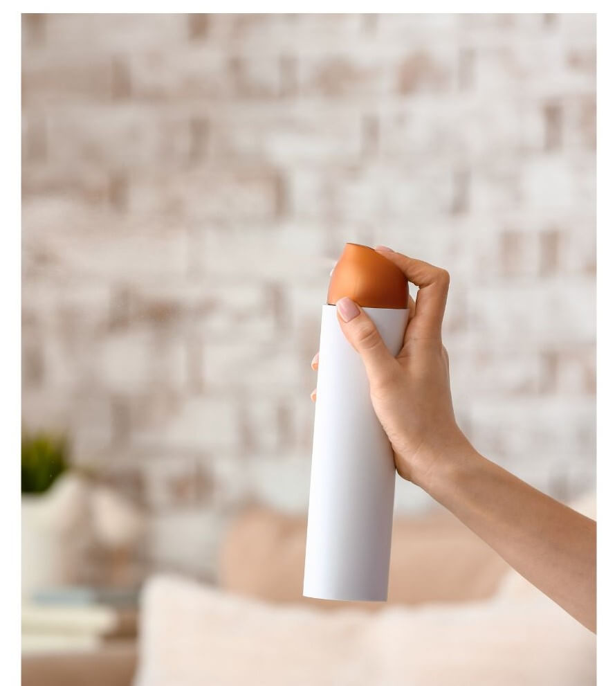 A hand holds a cylindrical white container with a brown top against a blurred indoor background.
