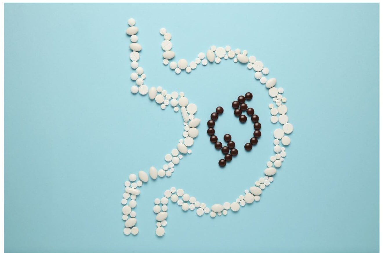 A configuration of white and brown pills arranged on a light blue background to illustrate the shape of a stomach.
