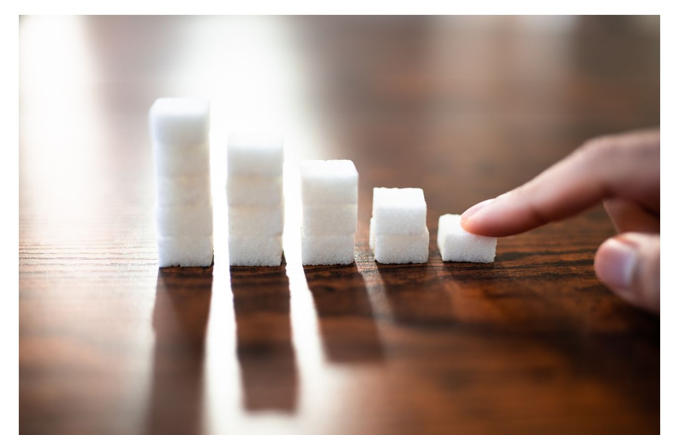 A finger is pointing at a small stack of sugar cubes arranged in increasing height on a wooden surface.