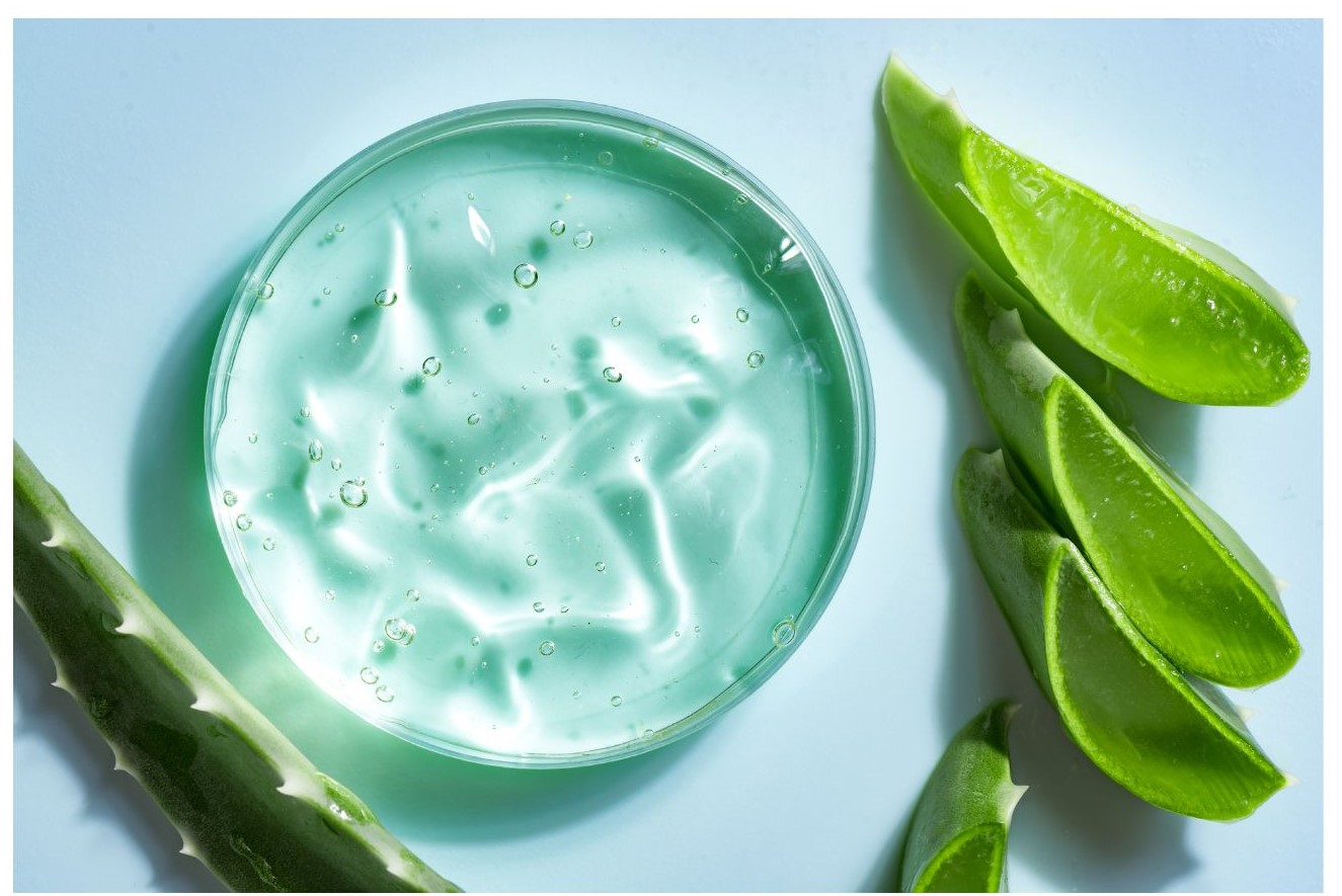 A clear, gel-like substance is surrounded by sliced green aloe vera leaves on a pale blue surface.