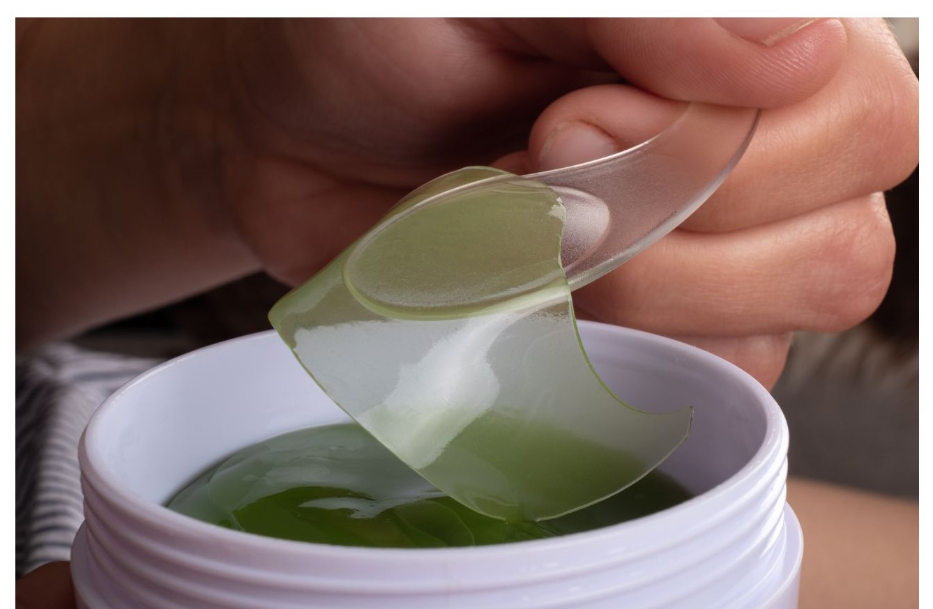 A hand is lifting a green gel patch out of a white container.