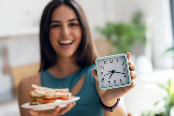 a woman with a clock and plate of food for fasting and cancer prevention