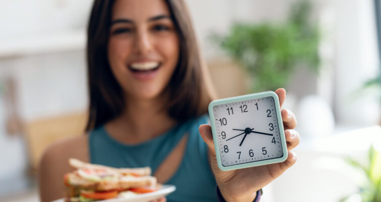 a woman with a clock and plate of food for fasting and cancer prevention