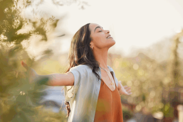 A woman joyfully stands with her arms outstretched, embracing the moment with a bright smile on her face.
