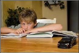 A young boy at a table, focused on a book, with a toy car placed next to him.