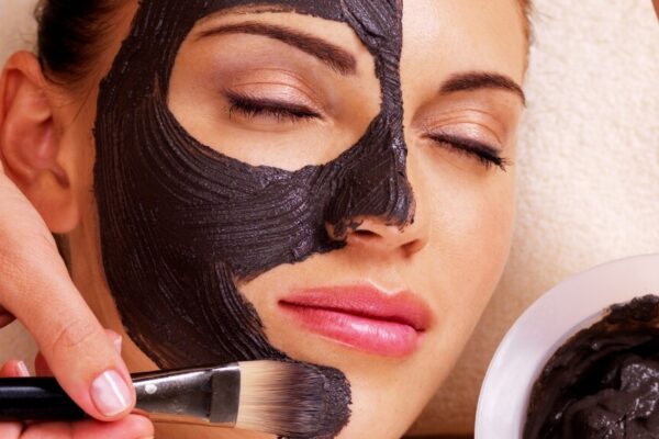 A woman applies black clay to her face, focusing on skincare and beauty treatment.