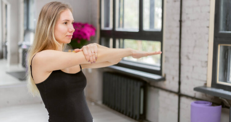 A woman stretches her arm in a serene yoga studio, demonstrating a yoga pose with focus and grace.