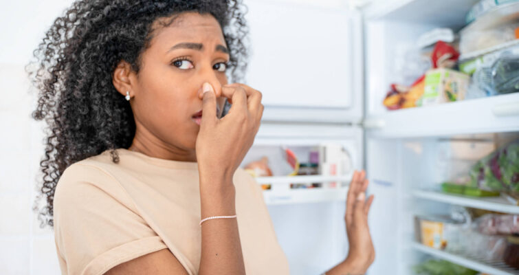 A woman stands in front of an open refrigerator, contemplating the overwhelming scents inside related to chemical sensitivity.