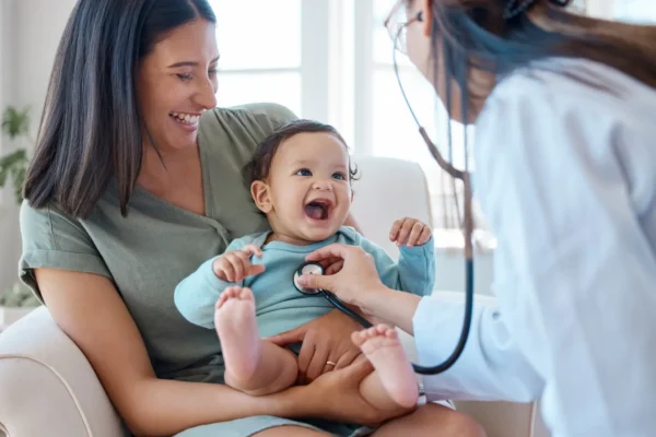 A woman holds a baby while a doctor examines the infant, highlighting integrative medicine therapies for children.
