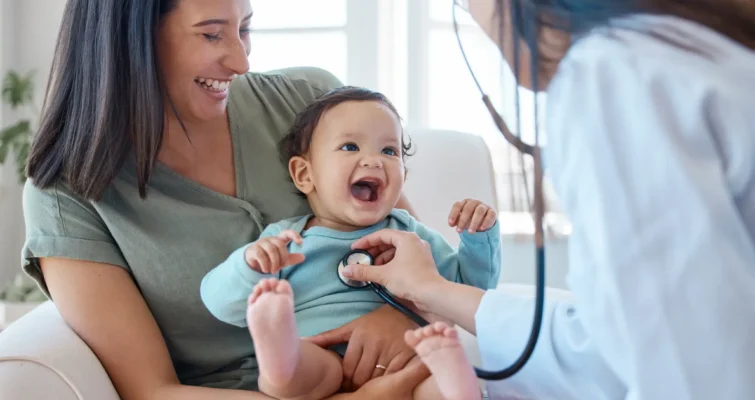 A woman holds a baby while a doctor examines the infant, highlighting integrative medicine therapies for children.