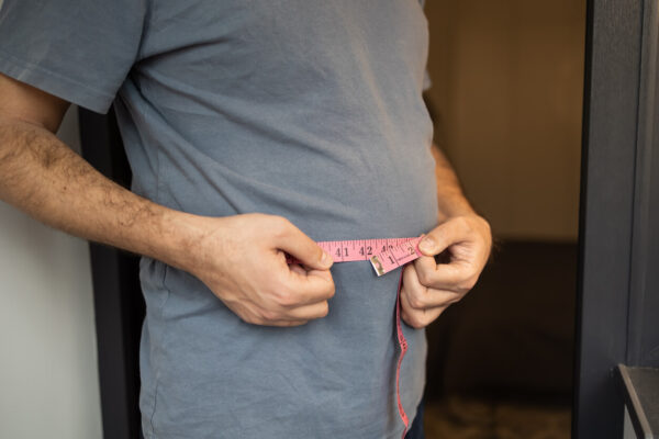 A man measures his waist with a tape measure, focusing on his fitness and health goals for obesity.