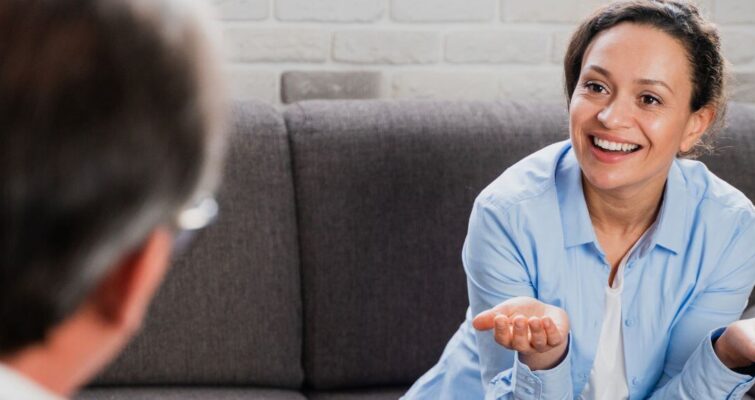 A woman sits on a couch, engaged in conversation with a man, discussing ADHD coaching options in Atlanta.