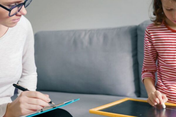 A woman and a child sit on a couch, focused on a tablet, illustrating a moment of shared learning about ADHD testing.