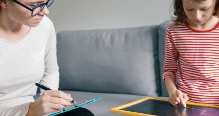 A woman and a child sit on a couch, focused on a tablet, illustrating a moment of shared learning about ADHD testing.