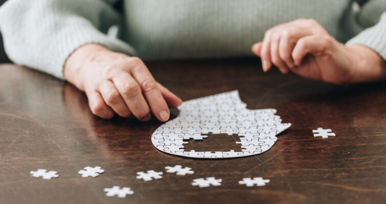 A woman assembles puzzle pieces on a table, symbolizing the complexities of Alzheimer's genetic testing.