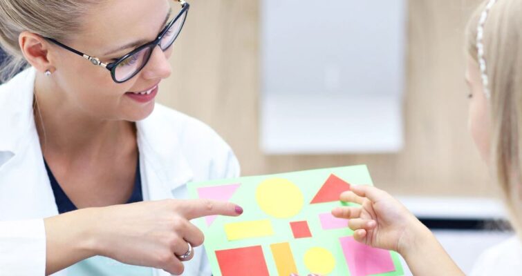 A woman in a lab coat assists a child with a puzzle, promoting engagement and learning in a supportive environment.