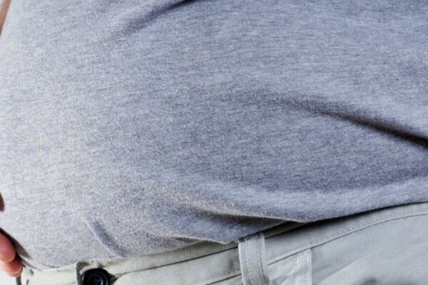 A man holds his stomach, possibly experiencing bloating, related to the topic of Berberine causes and remedies.