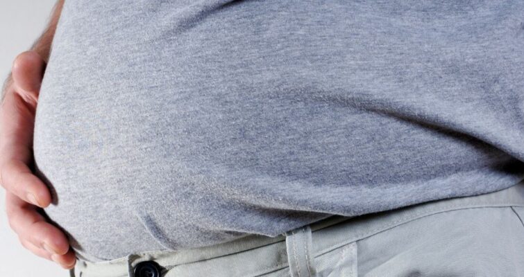 A man holds his stomach, possibly experiencing bloating, related to the topic of Berberine causes and remedies.