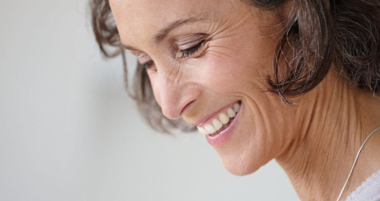 A woman smiling while looking at her phone, representing BioIdentical Hormone Therapy options in Atlanta.