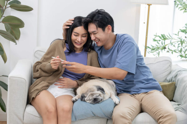 A young couple relaxes on a couch with a dog, enjoying each other's company in a cozy living room setting.