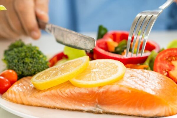 A person cuts into a plate of salmon and vegetables, showcasing a healthy meal option for women over 50.