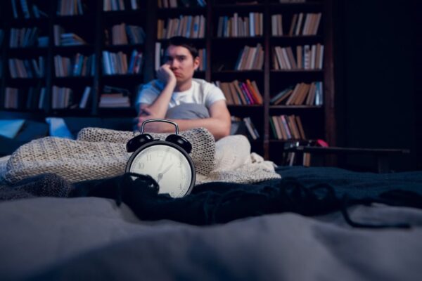 A man on a bed, appearing stressed, symbolizes anxiety and worries about not meeting expectations.