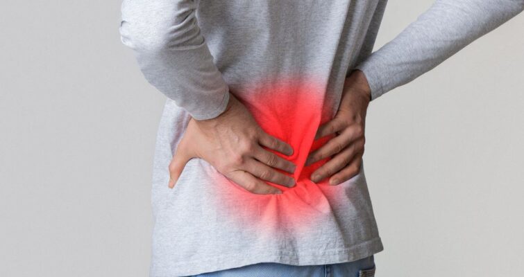 A man holding her lower back, indicating discomfort, related to hip pain and potential bone cancer concerns.