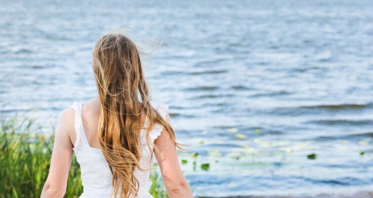A woman in a white dress stands by the water, symbolizing tranquility and balance in holistic hormone therapy.