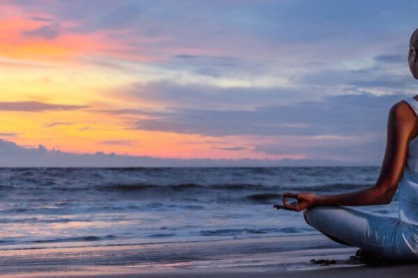 A woman meditates on the beach at sunset, promoting holistic health options in Atlanta.