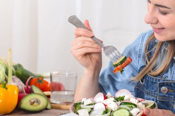 A woman enjoys a fresh salad with a fork, highlighting healthy eating for hormone balance in females.