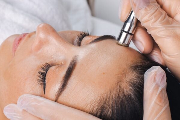 A woman sits in a salon chair while a beautician shapes her eyebrows with precision.