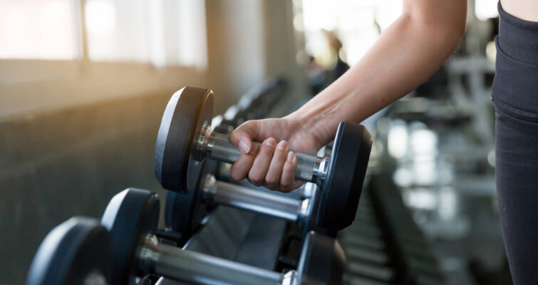 A woman holds a dumbbell while exercising in a gym, demonstrating strength and focus.