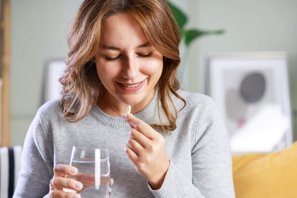 A woman smiles while holding a glass of water, conveying a sense of joy and refreshment.